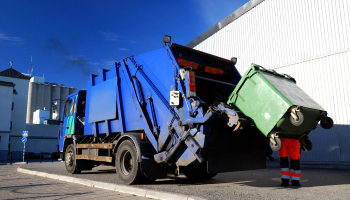 Man putting green garbage can into garbage truck